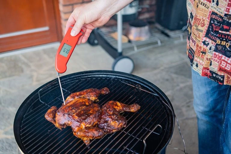 Člověk měří teplotu pečeného kuřete na grilu teploměrem.