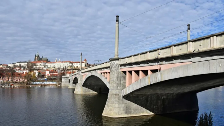 Historický železniční most přes Vltavu s Pražským hradem na pozadí.