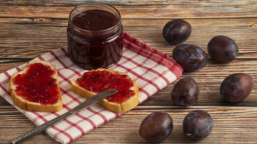 Sklenice povidla z meruněk s chlebem a čerstvé ovoce.